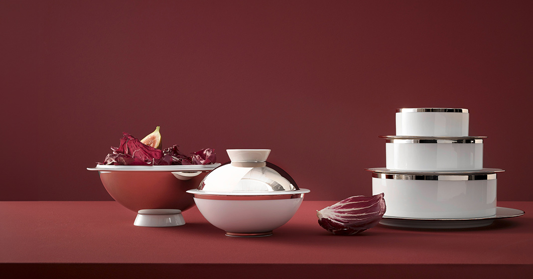 Porzellanschalen mit Radicchio gefüllt, daneben gestapelte Teller auf rotem Hintergrund. Fürstenberg Porzellan.