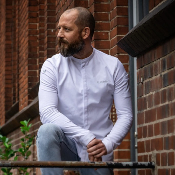 Mann im weißen Hemd kniet vor Backsteinwand, betrachtet seitlich. Fürstenberg Porzellan.