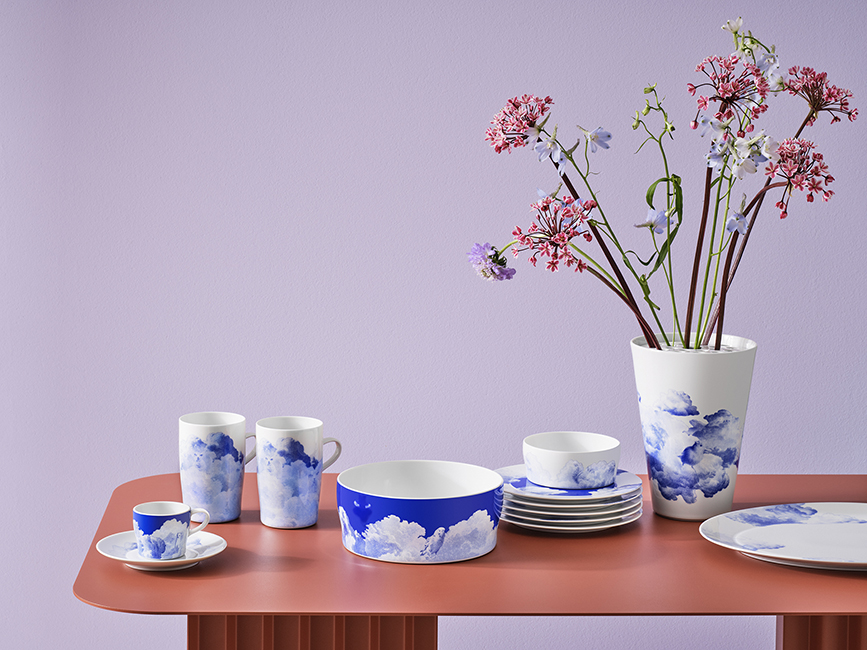 Porzellan Geschirr mit Wolkenmotiv auf rotem Tisch, Vase mit Blumen daneben. Fürstenberg Porzellan.
