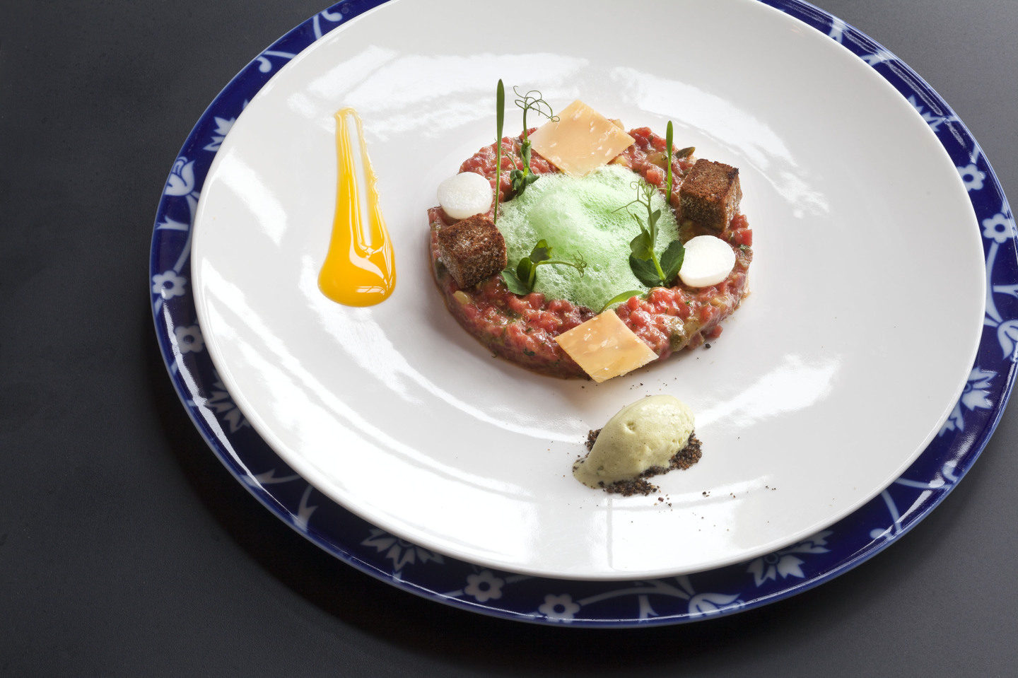 Kunstvoll angerichtetes Tatar mit grüner Espuma und Soße auf floralem Teller. Fürstenberg Porzellan.
