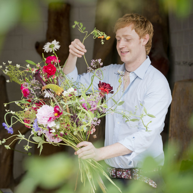 Person arrangiert bunte Blumen in einem Strauß, lächelnd im Freien. Fürstenberg Porzellan.
