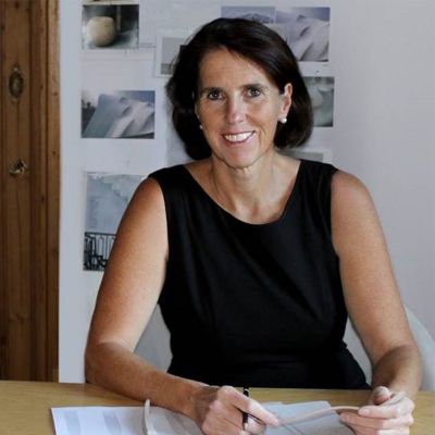 Eine Frau sitzt lächelnd am Schreibtisch und hält einen Stift. Fürstenberg Porzellan.