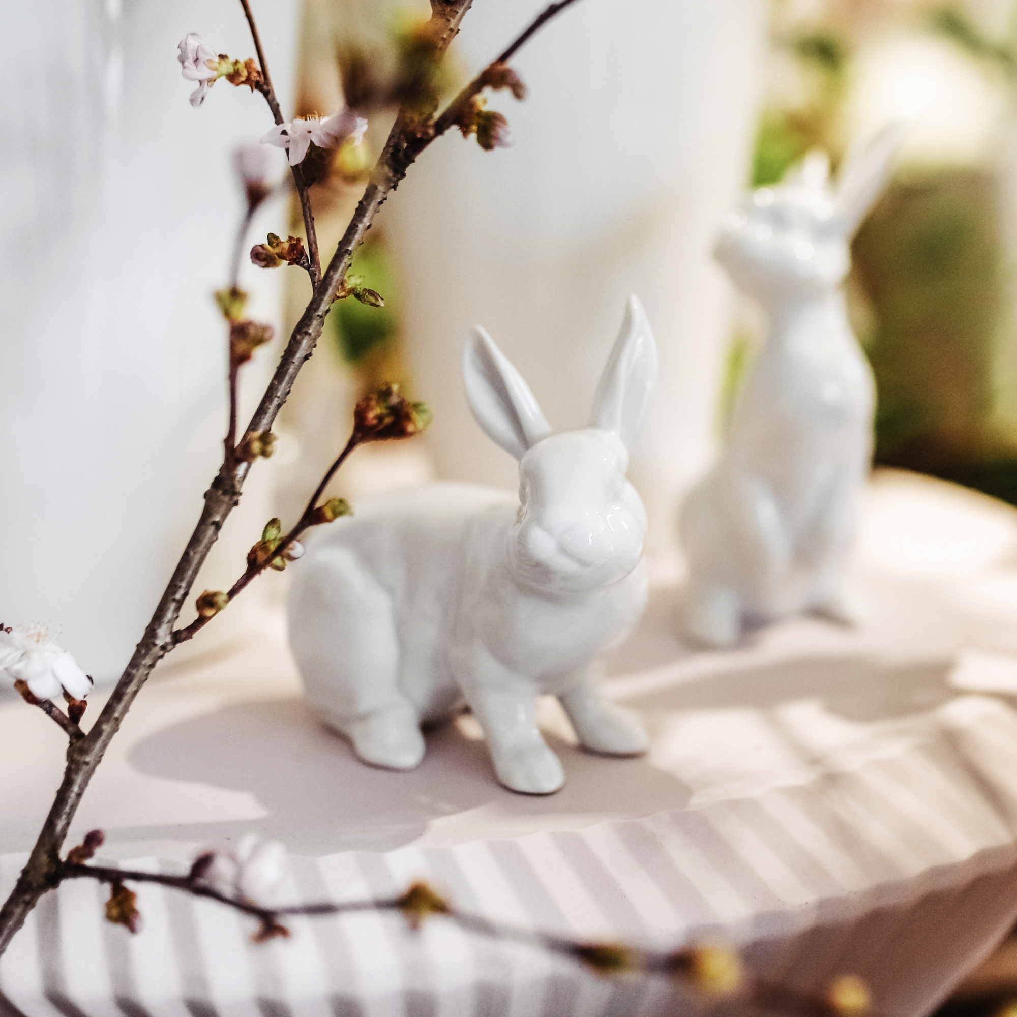 Porzellanfiguren Hasen sitzen neben blühendem Zweig auf gestreifter Oberfläche. Fürstenberg Porzellan.
