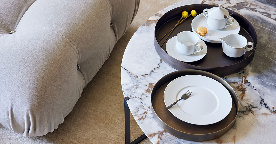 Marmortisch mit weißen Teetassen, Tellern und gelber Blume neben beigem Sofa. Fürstenberg Porzellan.