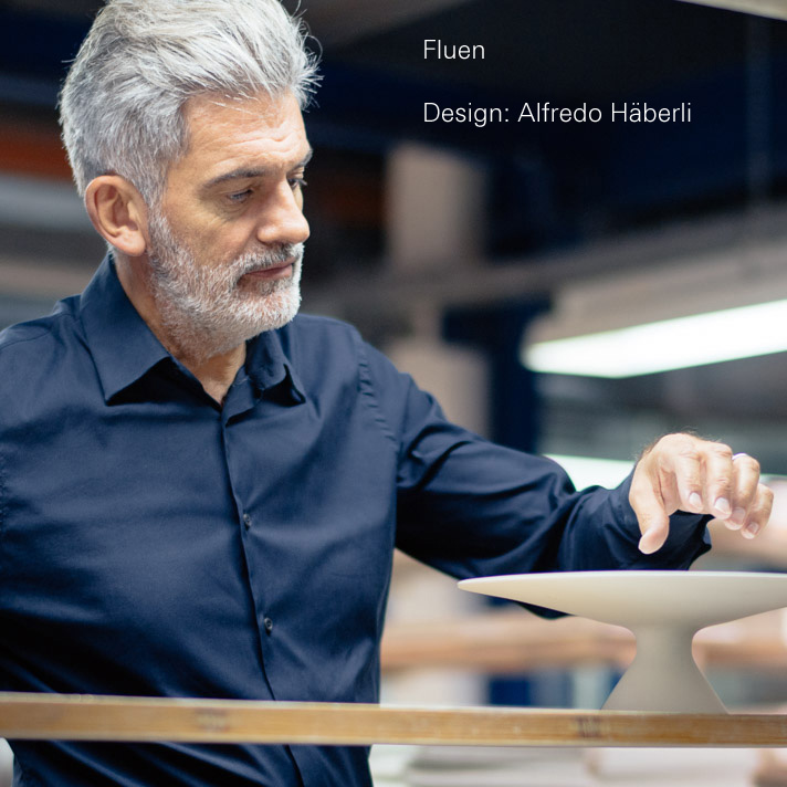 img3_fl2016327101_platzteller A man präsentiert elegantes Geschirrstück, modern gestaltet, in industrieller Umgebung. Text: "Fluen Design: Alfredo Häberli". Fürstenberg Porzellan.