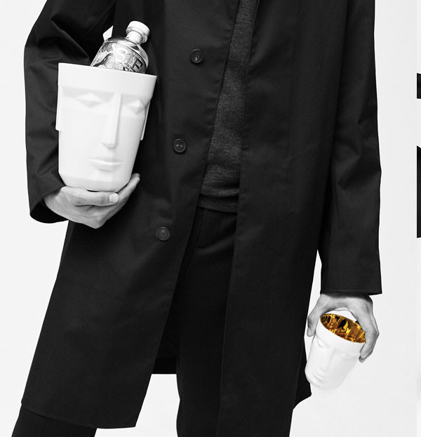 Person in schwarzem Mantel hält weiße Gefäße mit Gesichtsmotiv und Flasche. Fürstenberg Porzellan.