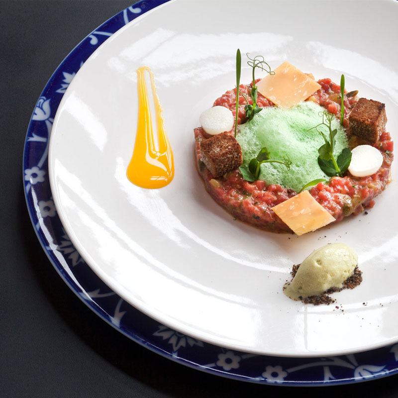 Tartar mit grüner Schaumhaube, Croutons und Saucendekoration auf weißem Teller. Fürstenberg Porzellan.