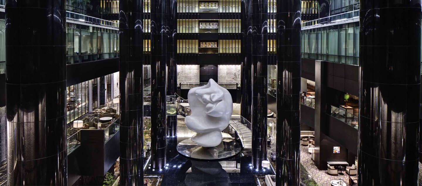 Weiße abstrakte Skulptur steht in modernem Atrium mit schwarzen Säulen. Fürstenberg Porzellan.