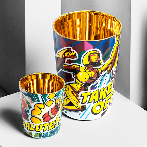 Zwei bunte Becher mit goldener Innenseite, zeigen Comic-Motiv und Text: "TAKE OFF" und "SALUTE!" Fürstenberg Porzellan.