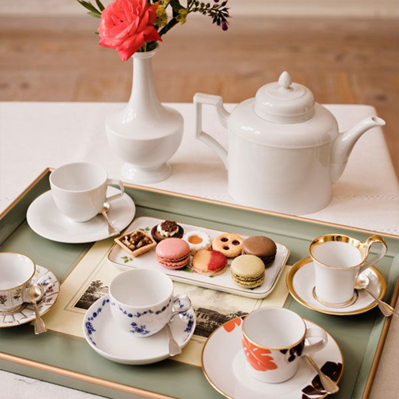 Tablett mit Porzellantassen, Teekanne und Macarons auf Tisch vor Blumenstrauß. Fürstenberg Porzellan.