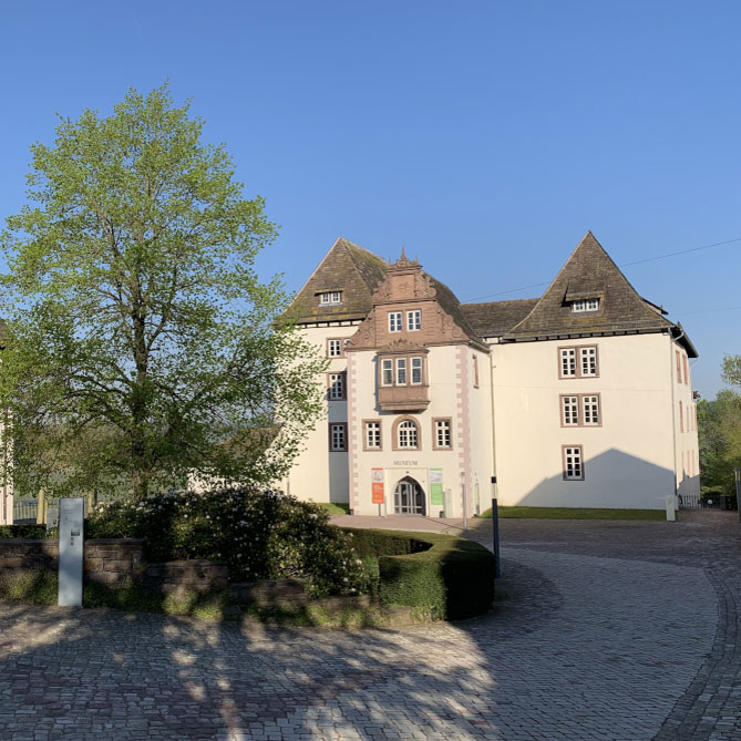 Weißes Schloss, umgeben von Bäumen, bei klarem Himmel. Fürstenberg Porzellan.