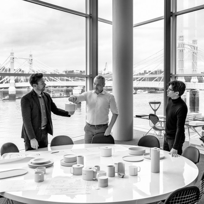 Drei Männer begutachten Porzellan am runden Tisch mit Brückenblick. Fürstenberg Porzellan.