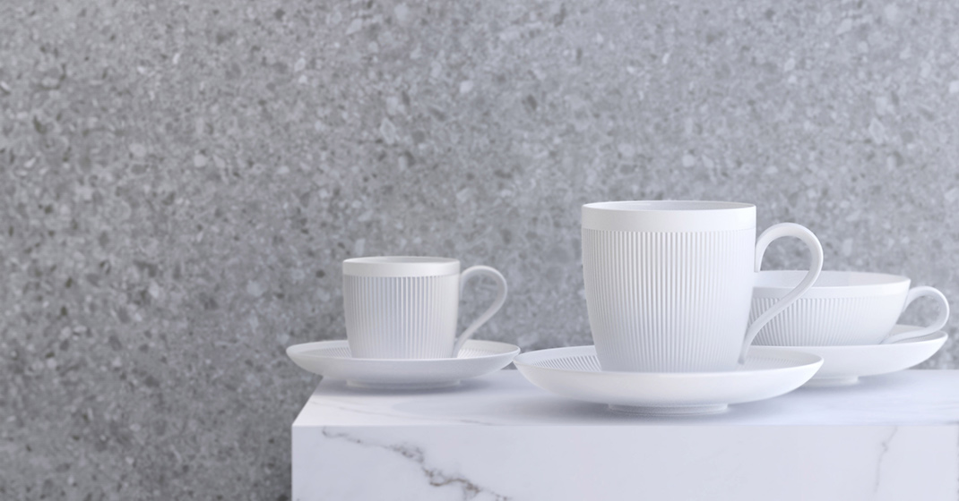Weiße Porzellantassen auf weißer Oberfläche vor grauer Steinwand. Fürstenberg Porzellan.